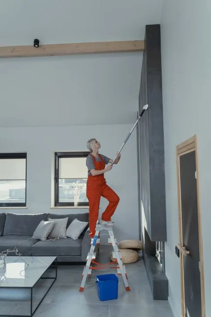 A woman carefully wraps a sofa in protective material while packing boxes in a bright room.